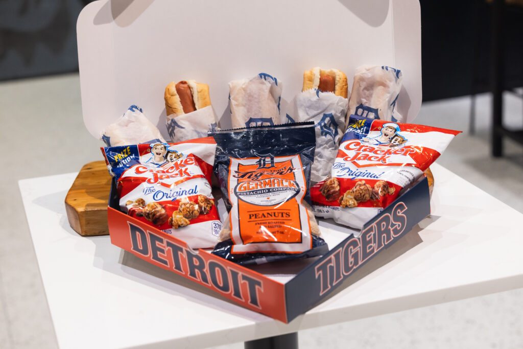 A Detroit Tigers-themed snack box containing hot dogs, Cracker Jack, and peanuts.