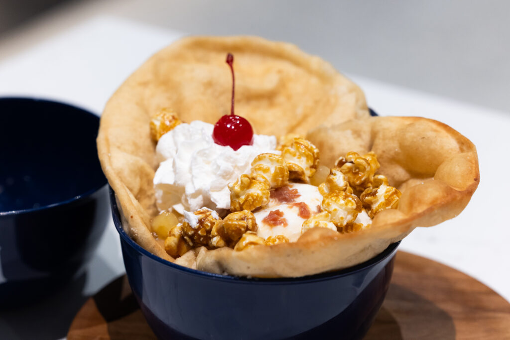 A caramel popcorn sundae topped with whipped cream and a cherry, served in a crispy fried pastry bowl.